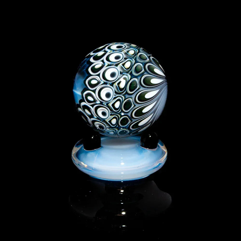 Handcrafted glass marble with intricate black, white, and green pattern on a blue base