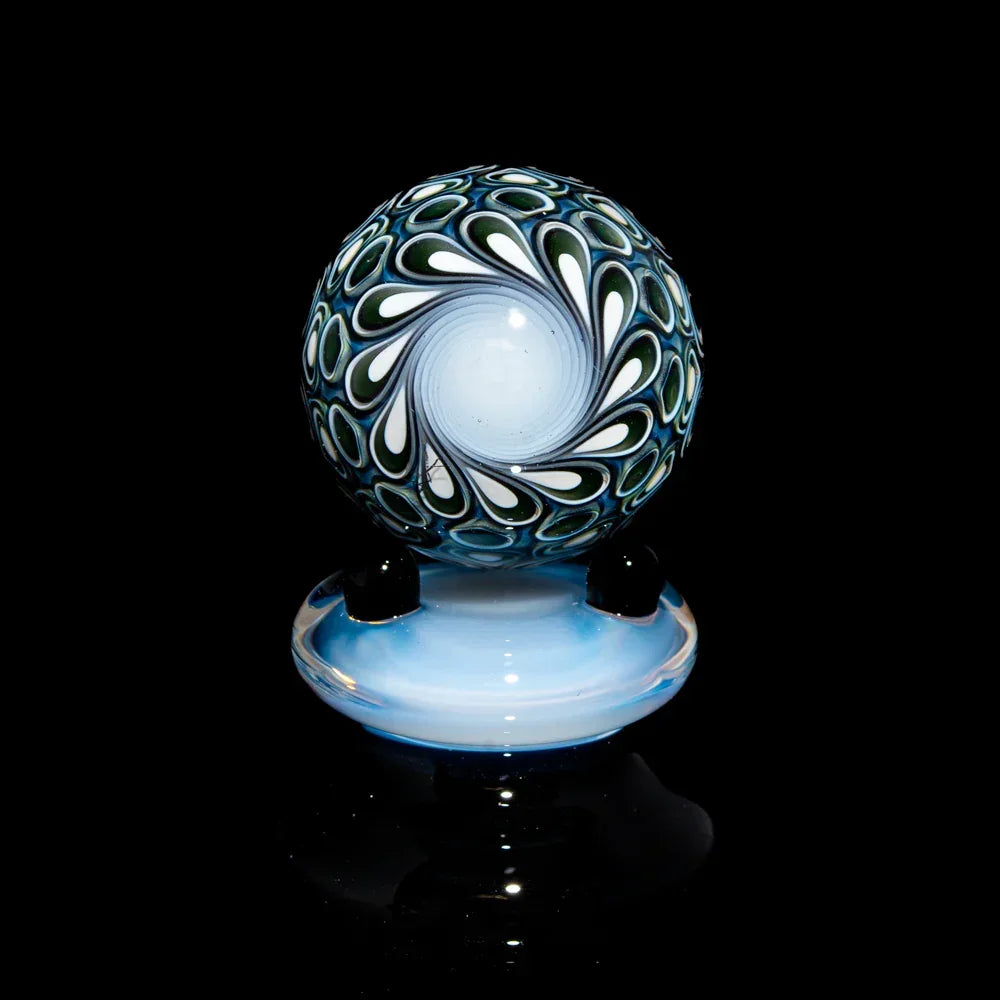 Hand-blown glass marble with intricate blue, white, and black swirl pattern on a stand