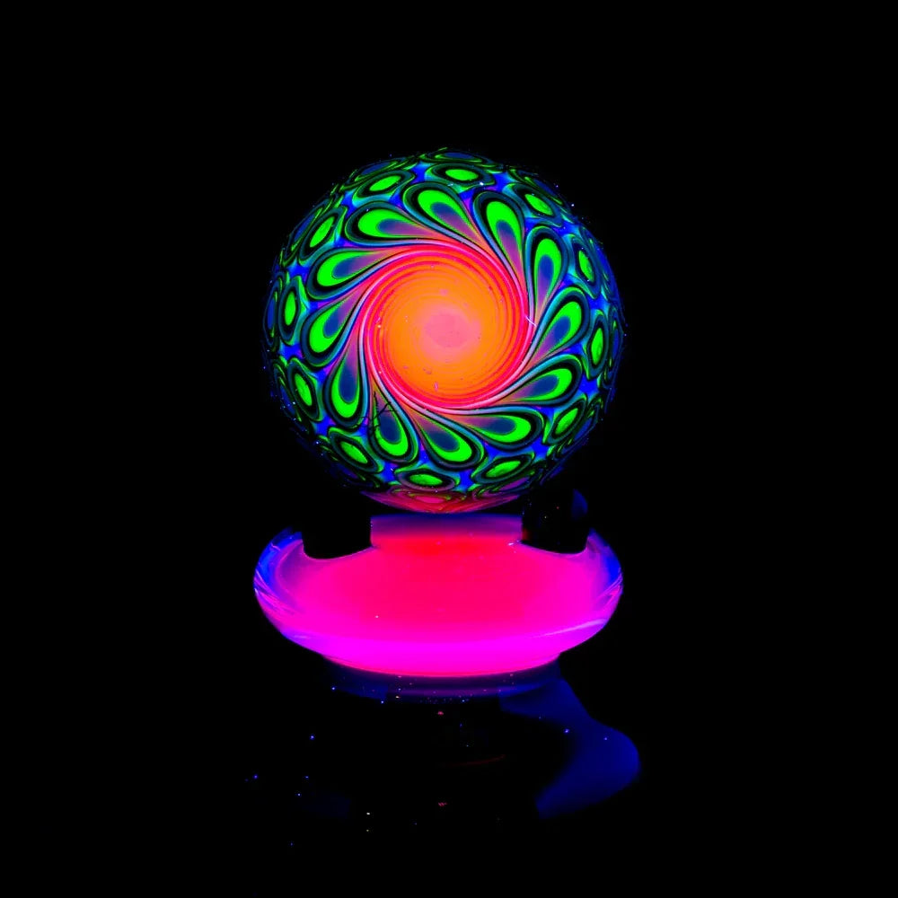 Colorful psychedelic glass marble with neon green and orange swirl pattern, glowing under blacklight.