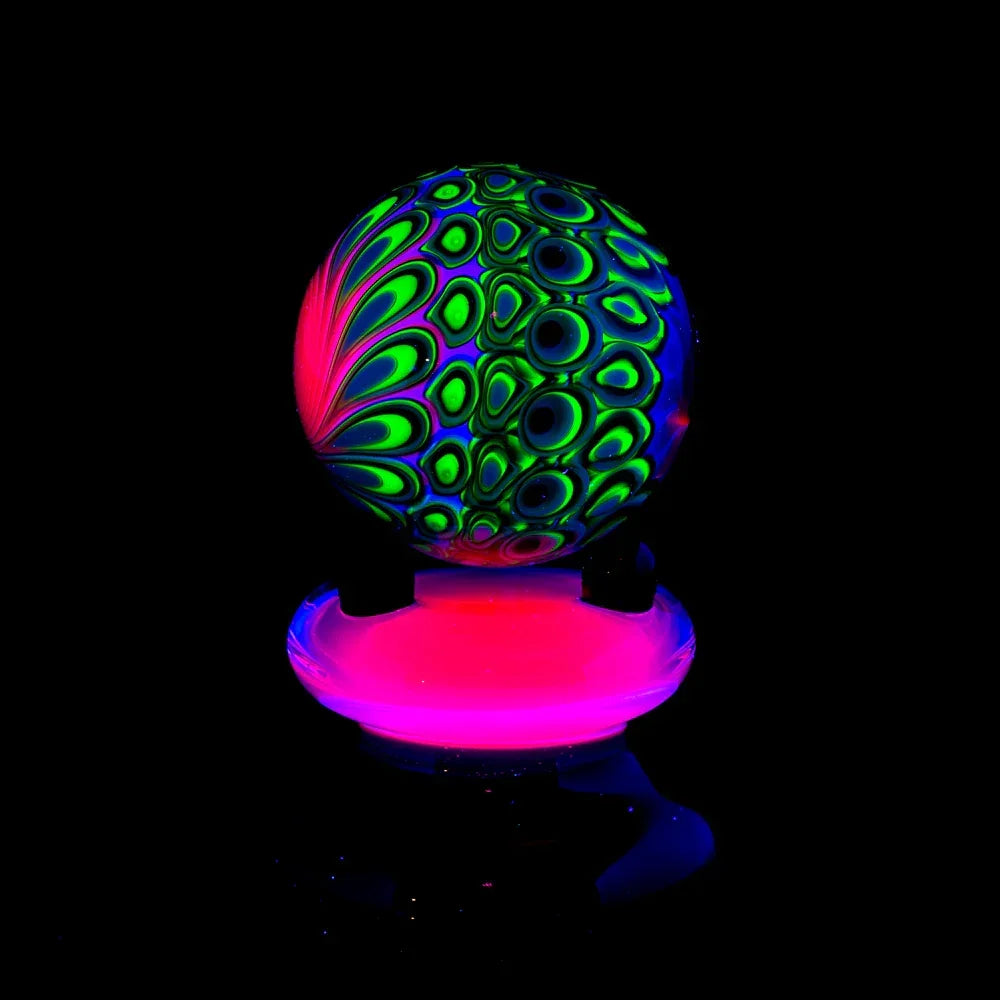UV reactive glass marble with neon green and pink patterns on a glowing stand