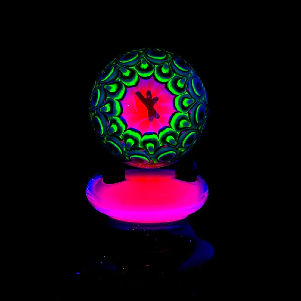 UV reactive glass marble with intricate green and black patterns on a glowing pink stand