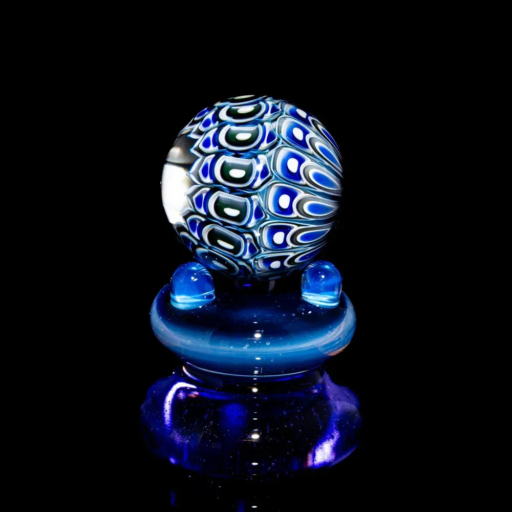 Colorful hand-blown glass marble with intricate blue, green, and white patterns on black background