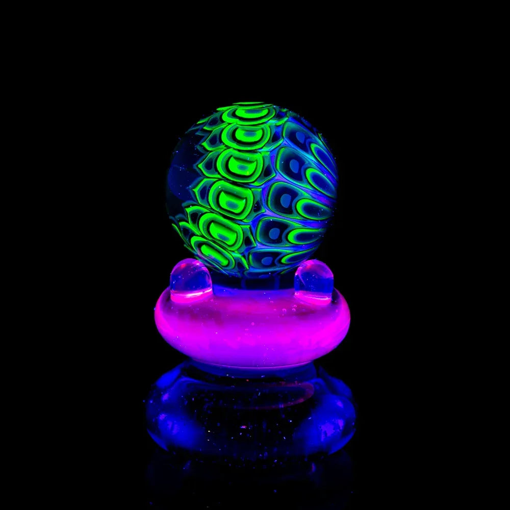 UV reactive glass marble with green and blue patterns, glowing on a purple and blue stand