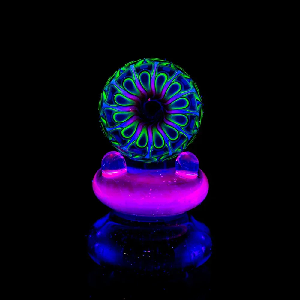 UV reactive glass marble with vibrant neon green, purple, and blue patterns on black background