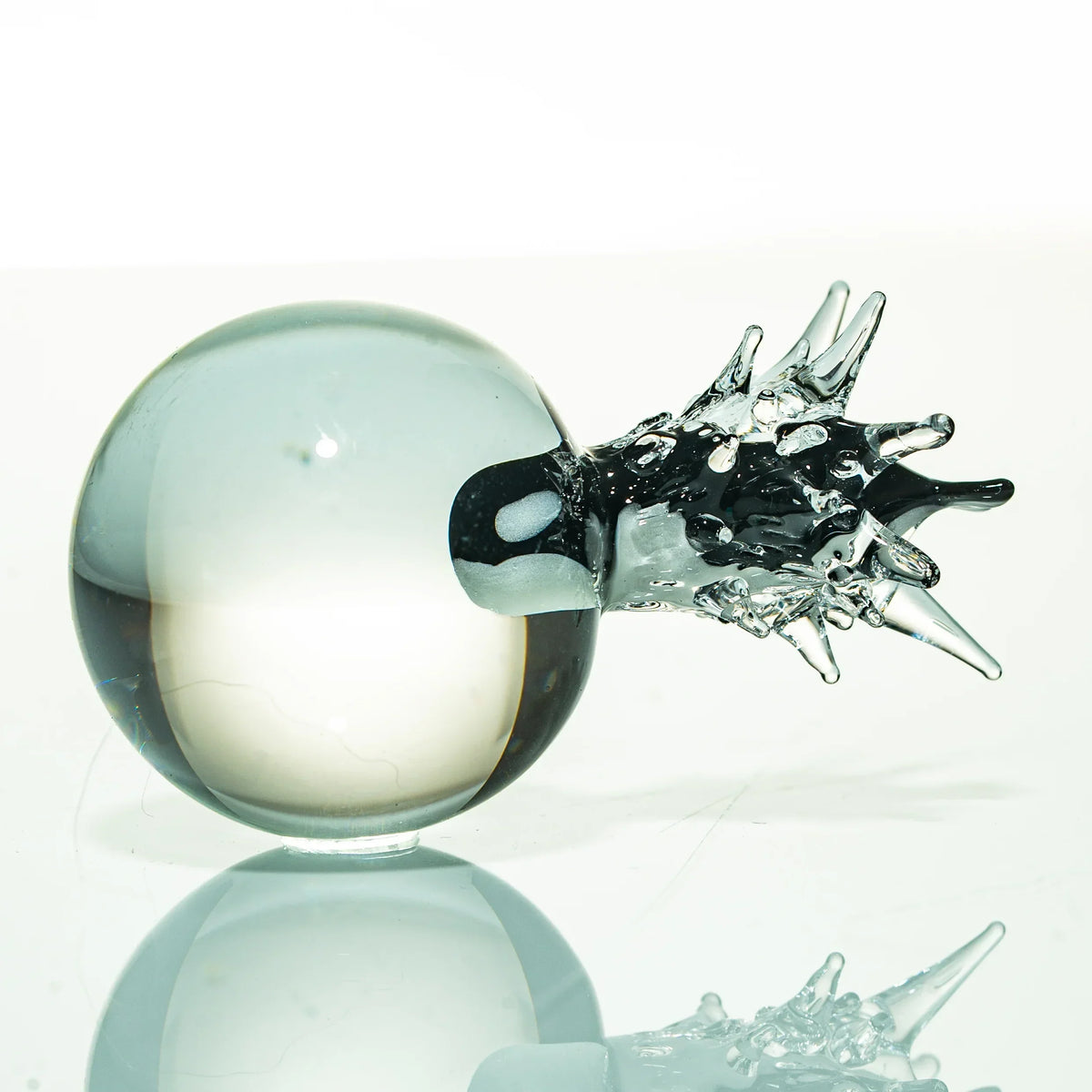 Clear art glass sphere with spiked detail, displayed on reflective surface