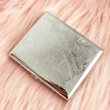 Silver engraved metal case with floral pattern on pink faux fur background
