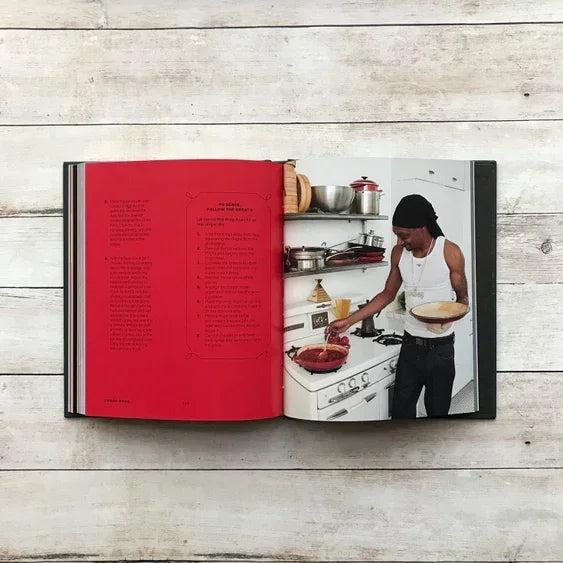 Open cookbook with red recipe page and man cooking in kitchen on wood table background