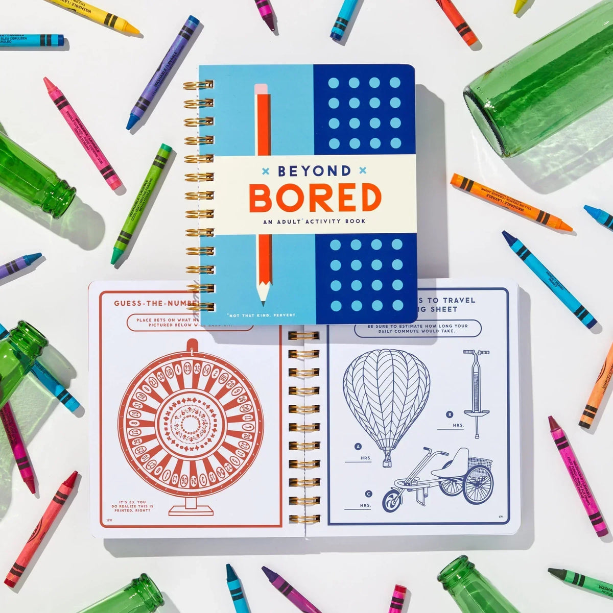 Beyond Bored adult activity book with colorful crayons and green glass bottles on white table.
