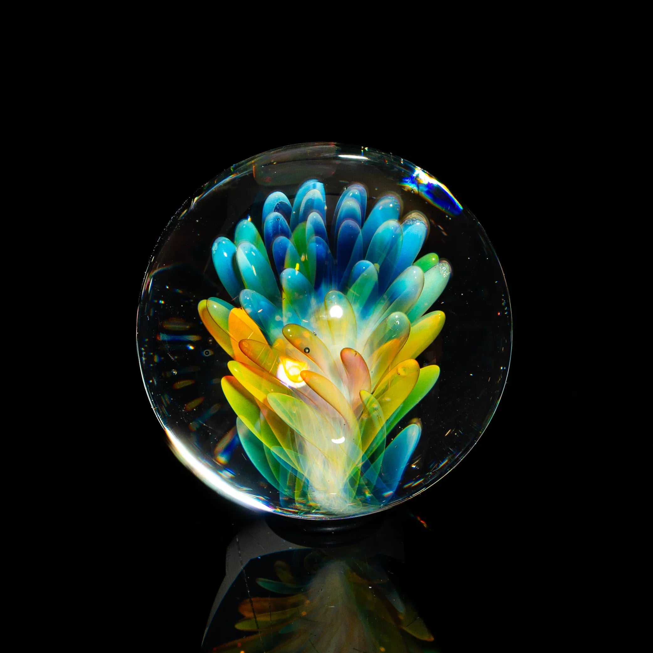 Colorful glass art marble with vibrant blue, yellow, and green petals on black background