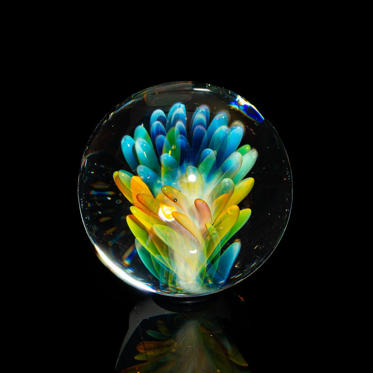 Colorful glass art marble with vibrant blue, yellow, and green petals on black background
