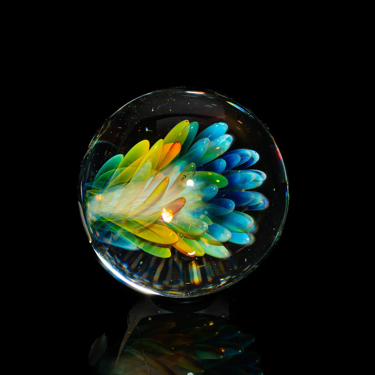 Hand-blown glass marble with vibrant blue, green, and yellow floral design on black background