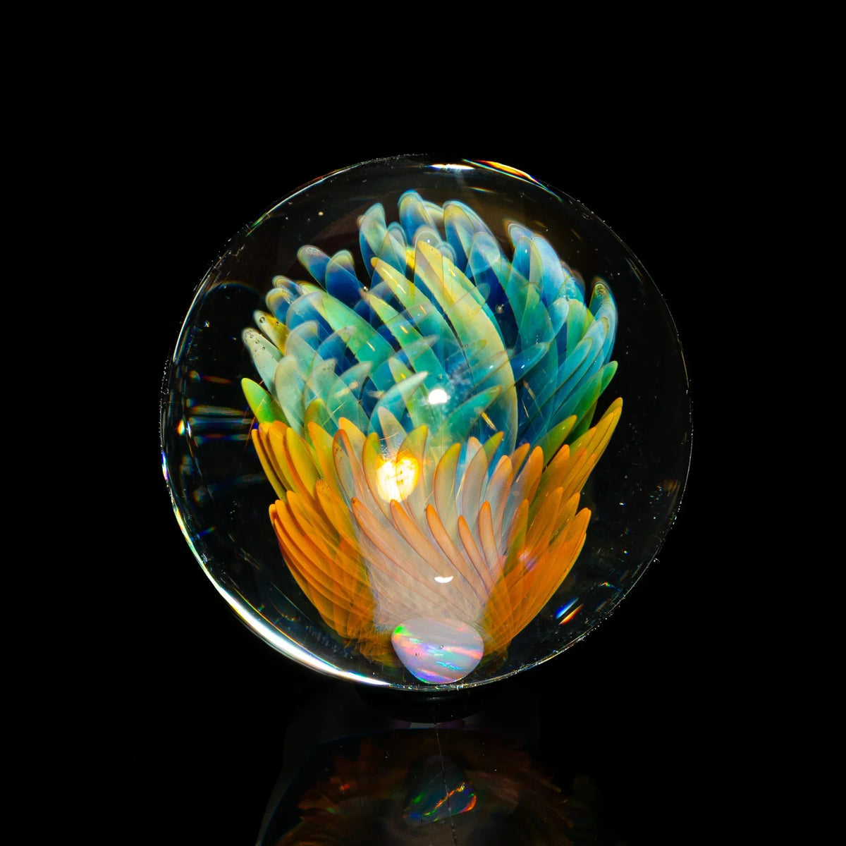 Handcrafted glass marble with colorful blue and orange feather-like patterns on black background.