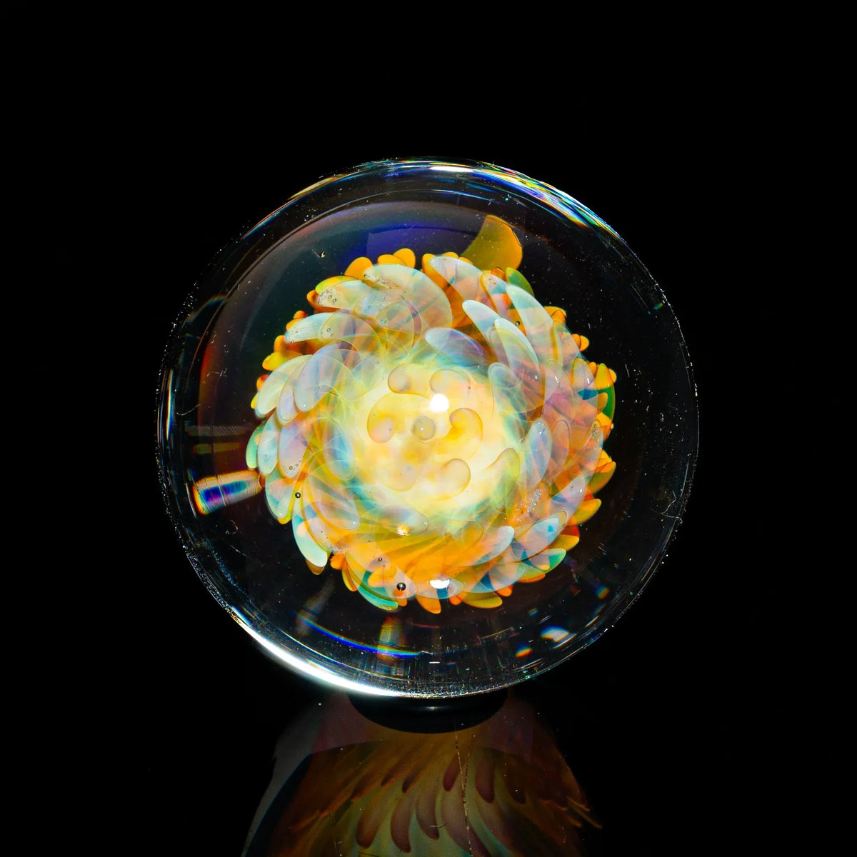 Hand-blown glass marble with intricate orange and yellow flower design on black background