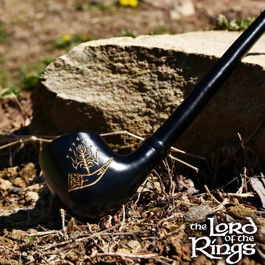 Black Lord of the Rings themed pipe with gold emblem resting on dirt and rocks outdoors