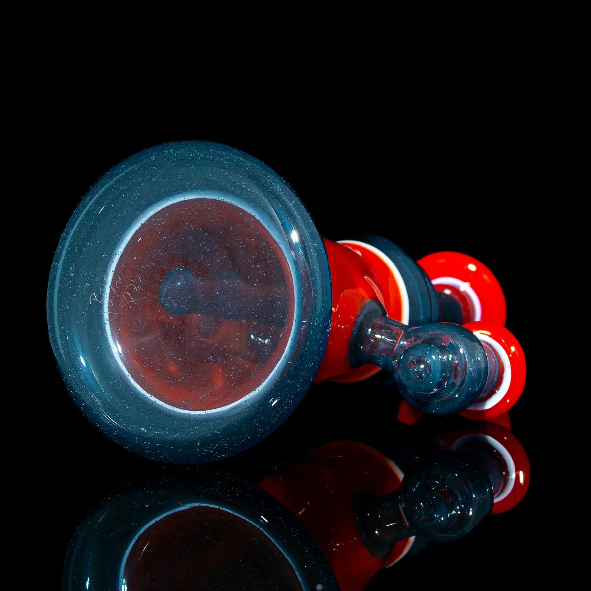 Red and black heady glass pipe with intricate design on a black reflective surface