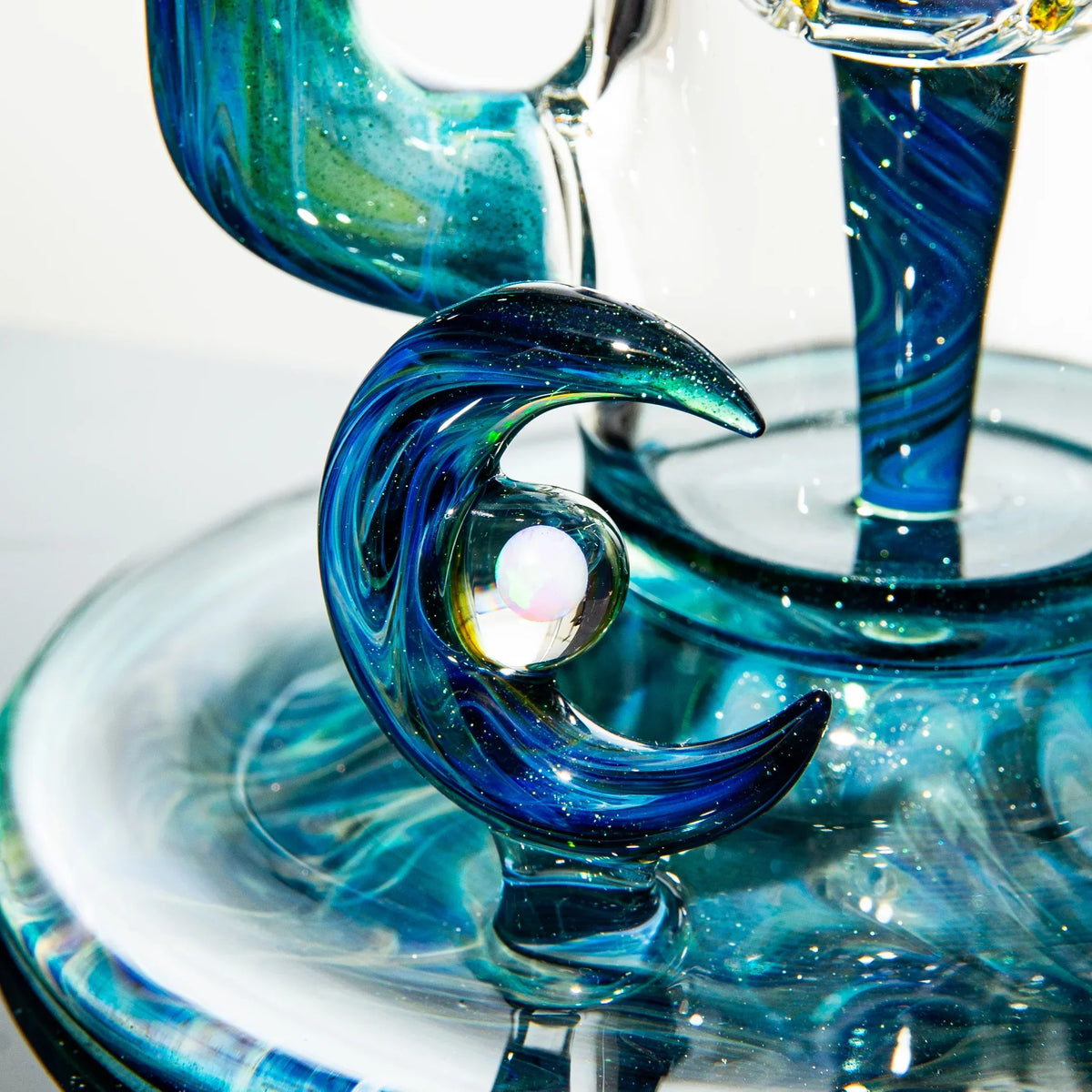 Close-up of artistic blue glass water pipe with crescent moon detail and opal marble