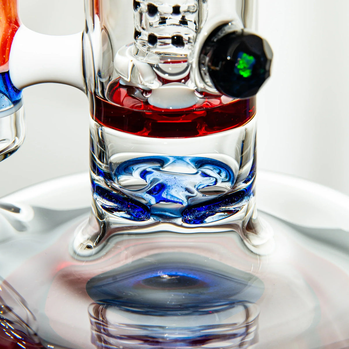 Close-up of a heady glass water pipe base with blue and red accents and opal detail.
