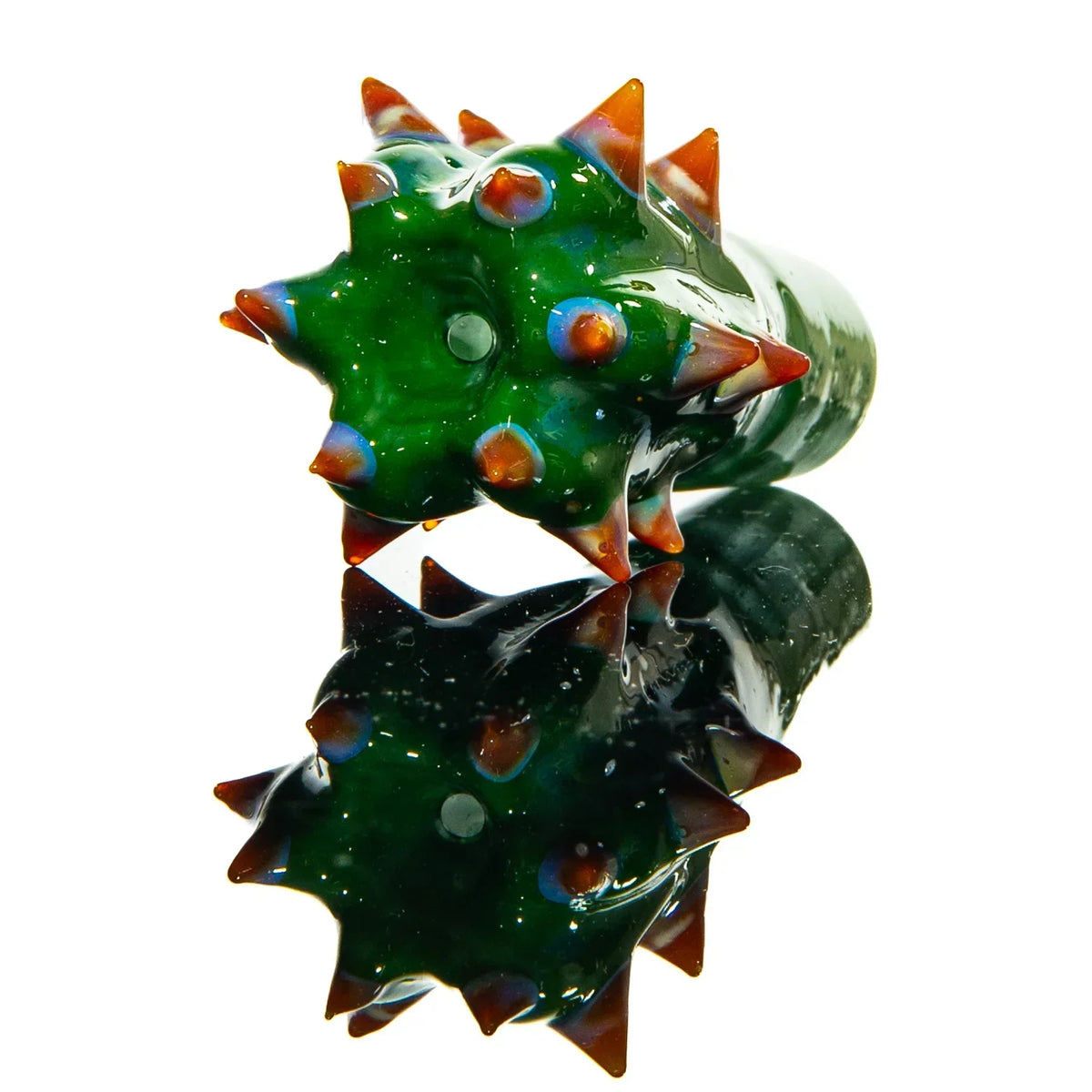 Green glass cactus-shaped accessory with orange spikes on white reflective surface