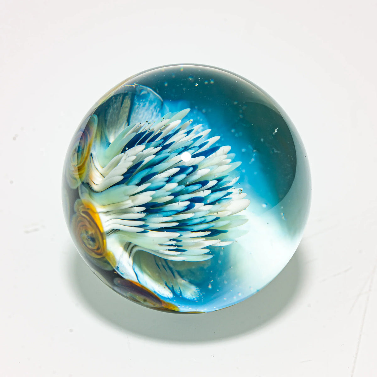 Handcrafted glass marble with blue and white flower petal design on a white background