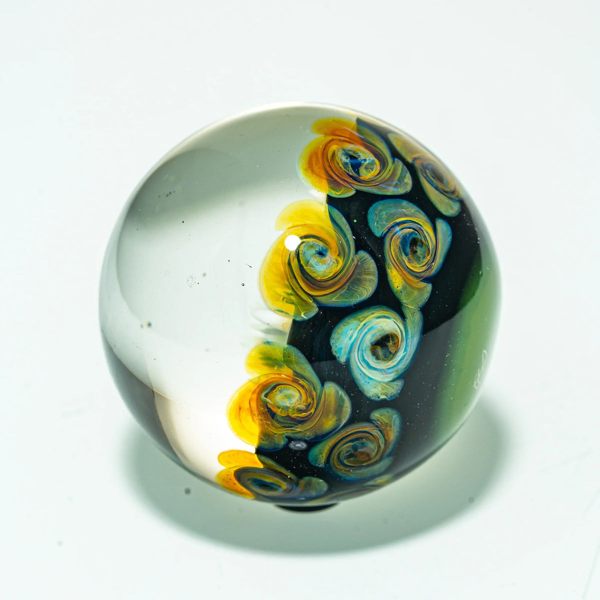 Hand-blown glass marble with intricate yellow and blue floral swirl patterns