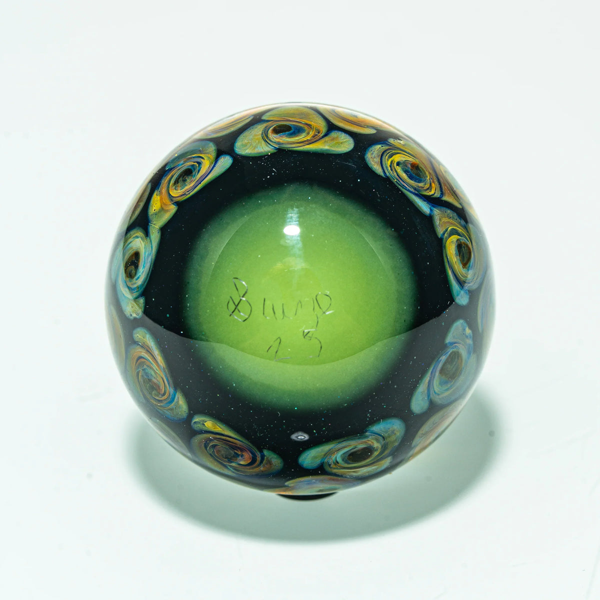 Handcrafted glass marble with green center and colorful swirl accents on white background