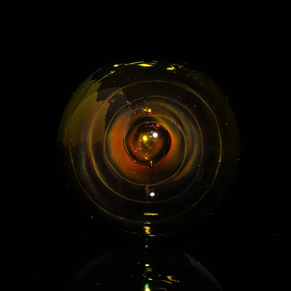 Handcrafted amber heady glass marble with spiral design on black background