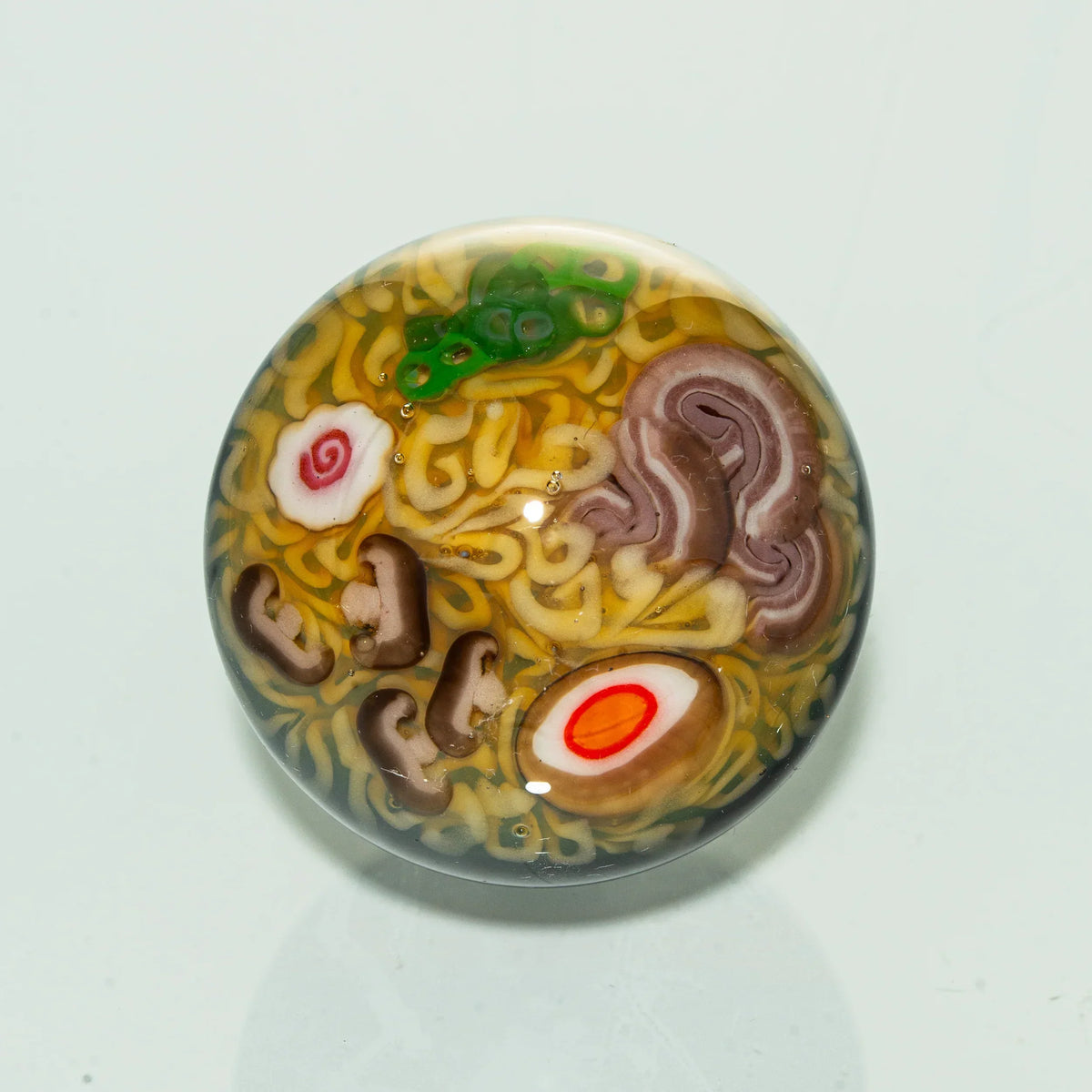Glass marble with realistic ramen noodle, egg, mushroom, and green garnish design.