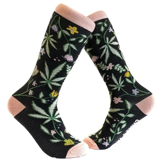 Black crew socks with cannabis leaf and floral pattern, pink toe and heel accents.