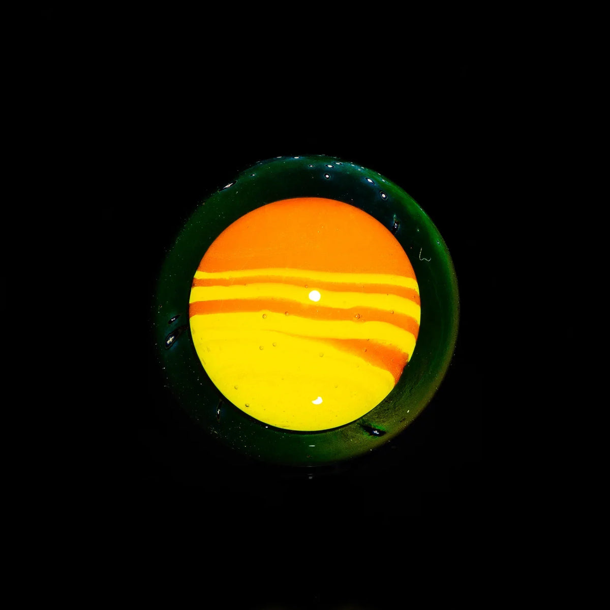 Handblown glass marble with vibrant orange and yellow swirl design on black background