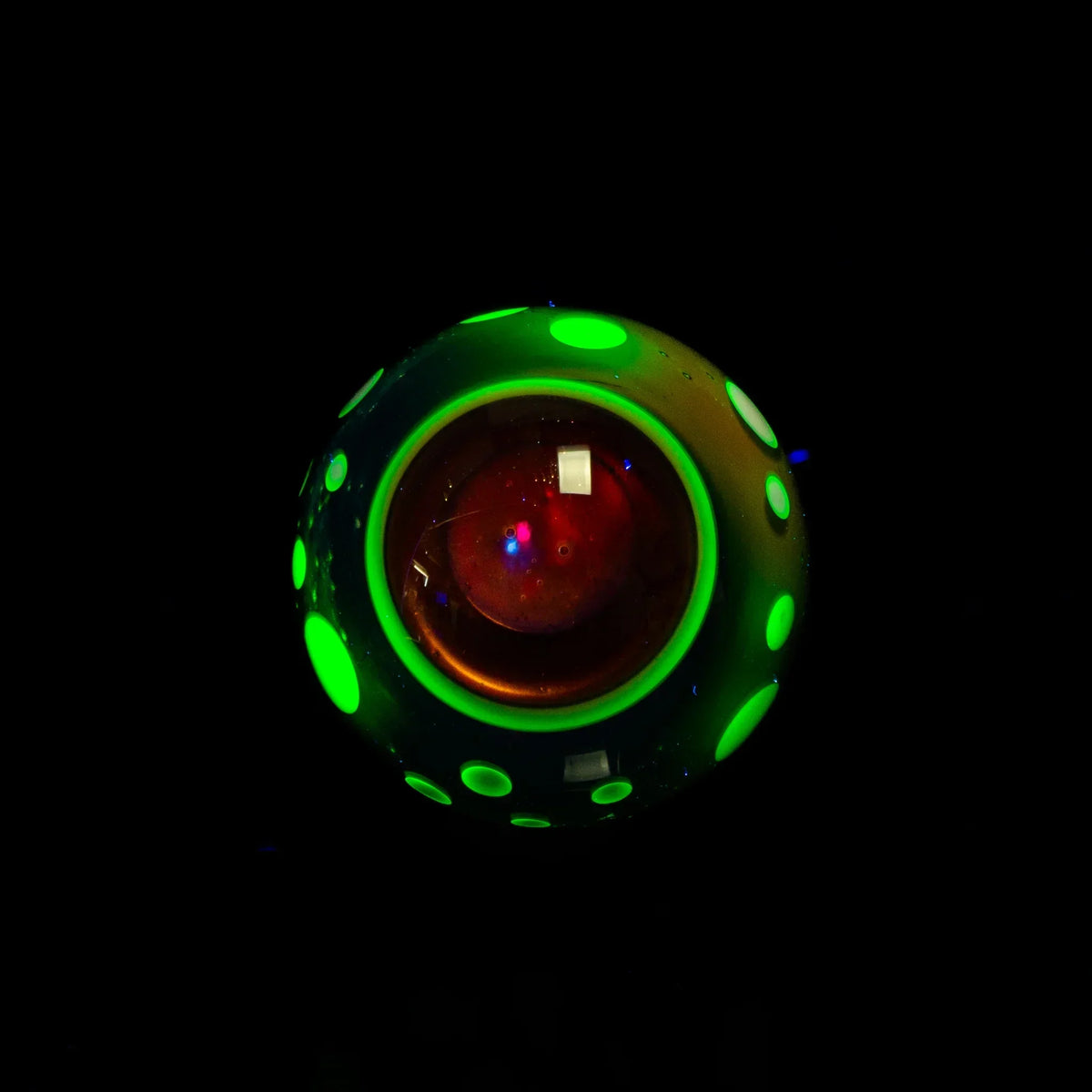 Glowing glass marble with neon green dots and red core on black background