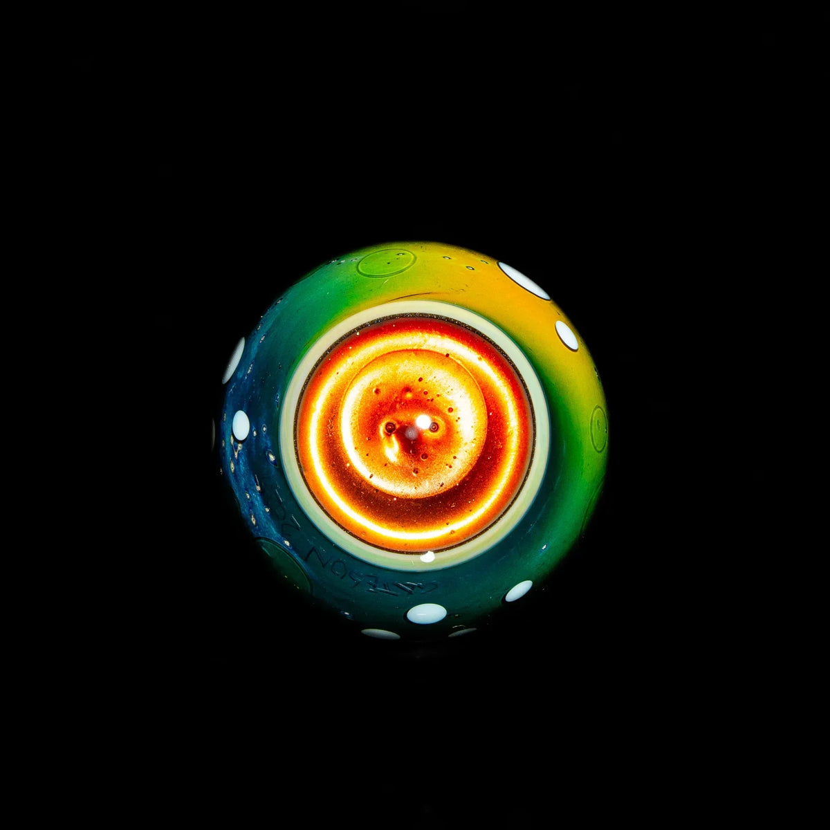 Colorful heady glass marble with spiral design and white polka dots on black background