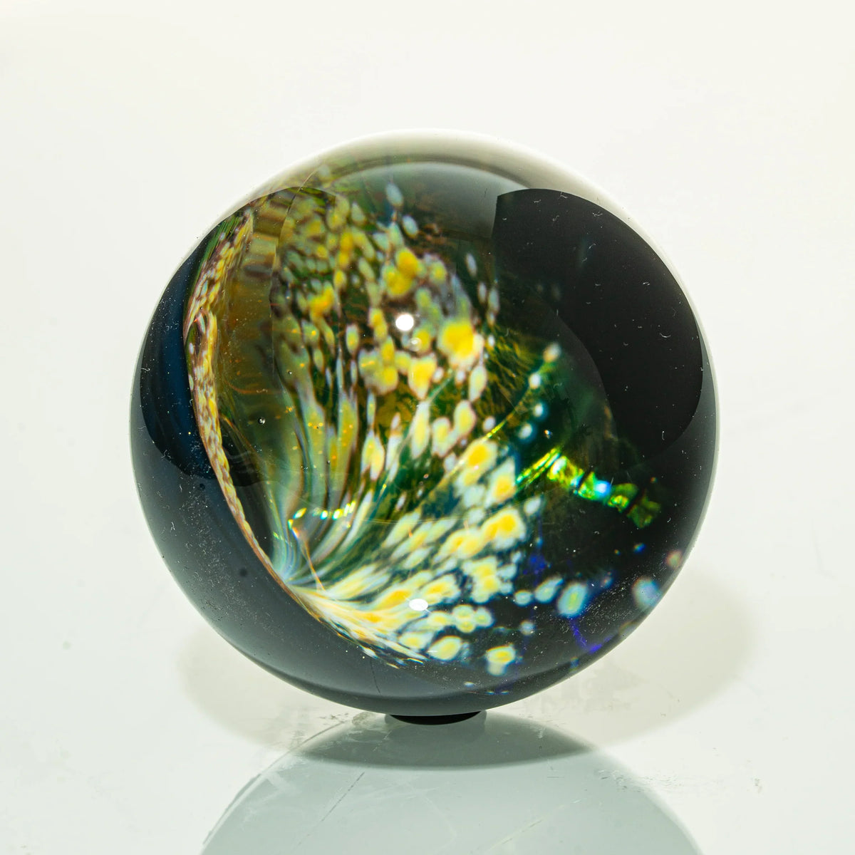 Handcrafted glass marble with swirling yellow, white, and green patterns on a glossy surface