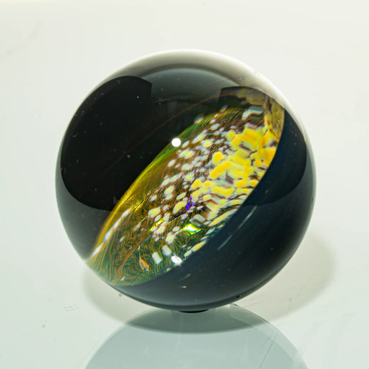 Art glass marble with black exterior and colorful, intricate yellow and white pattern inside