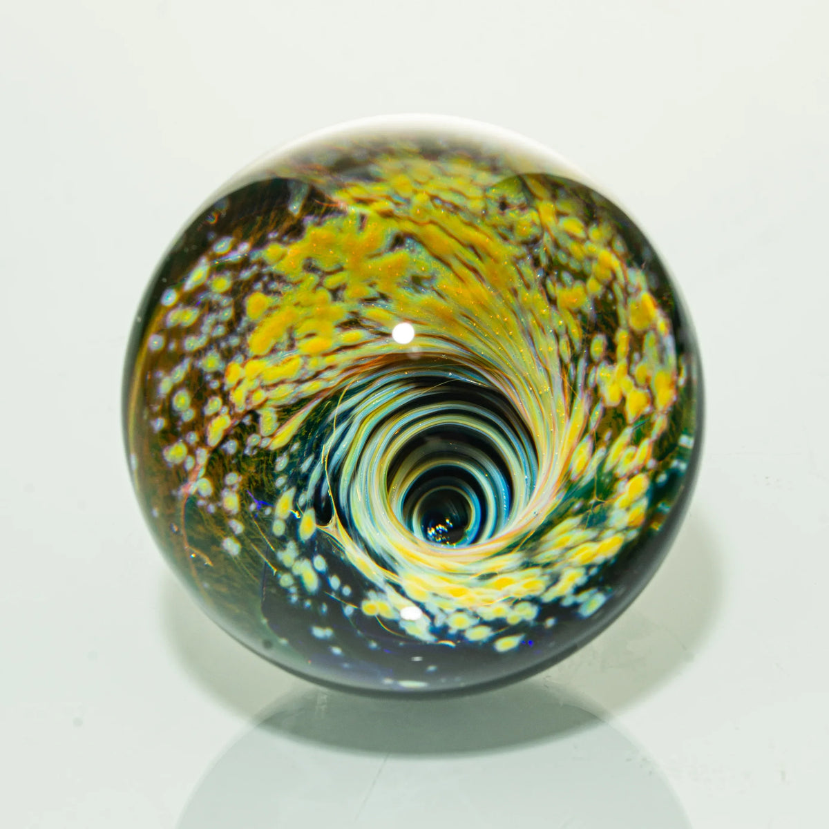 Hand-blown glass marble with swirling yellow and blue vortex design on white background