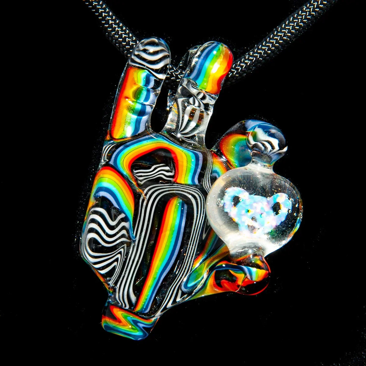 Rainbow striped glass pendant shaped like a hand with orb and bear design, on a black cord