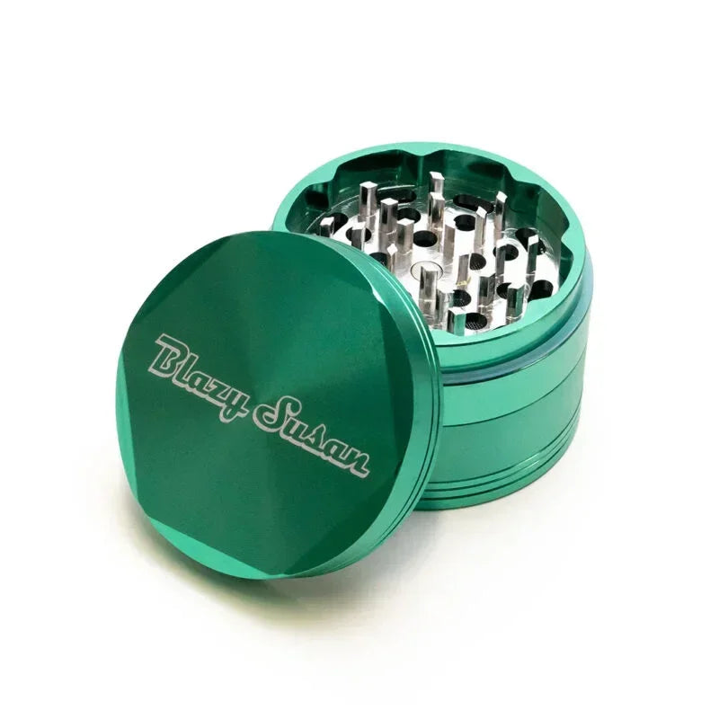 Green metal herb grinder with open lid and sharp teeth, Blazy Susan engraving visible.