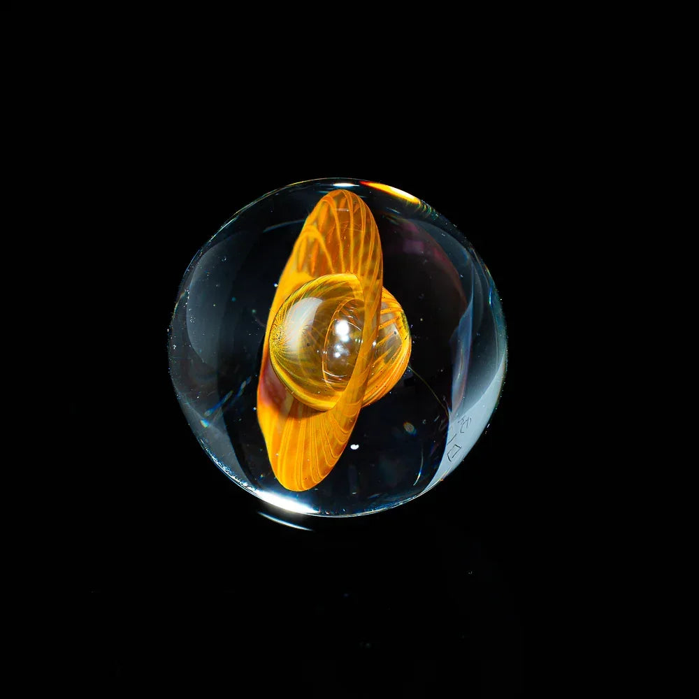 Handcrafted glass marble with orange swirled core on black background