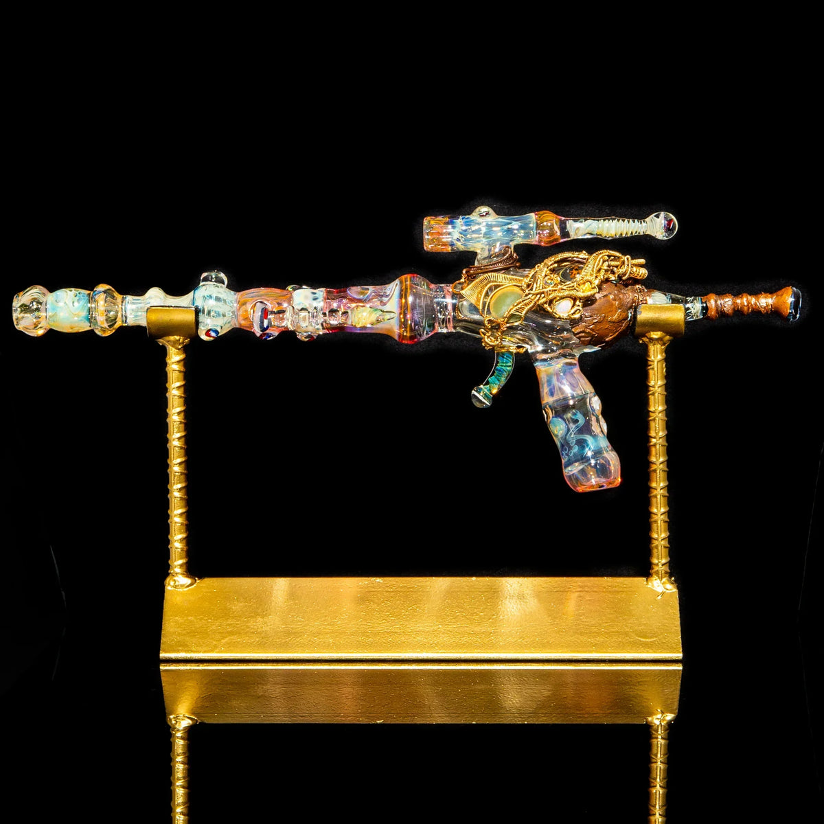 Colorful heady glass pipe shaped like a rifle displayed on a gold stand, black background