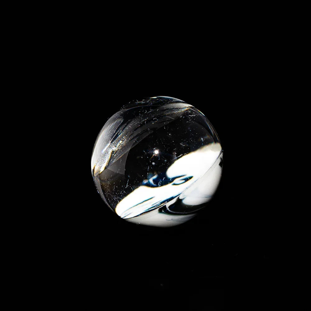 Clear glass marble with milky swirl design on black background, glass accessory closeup
