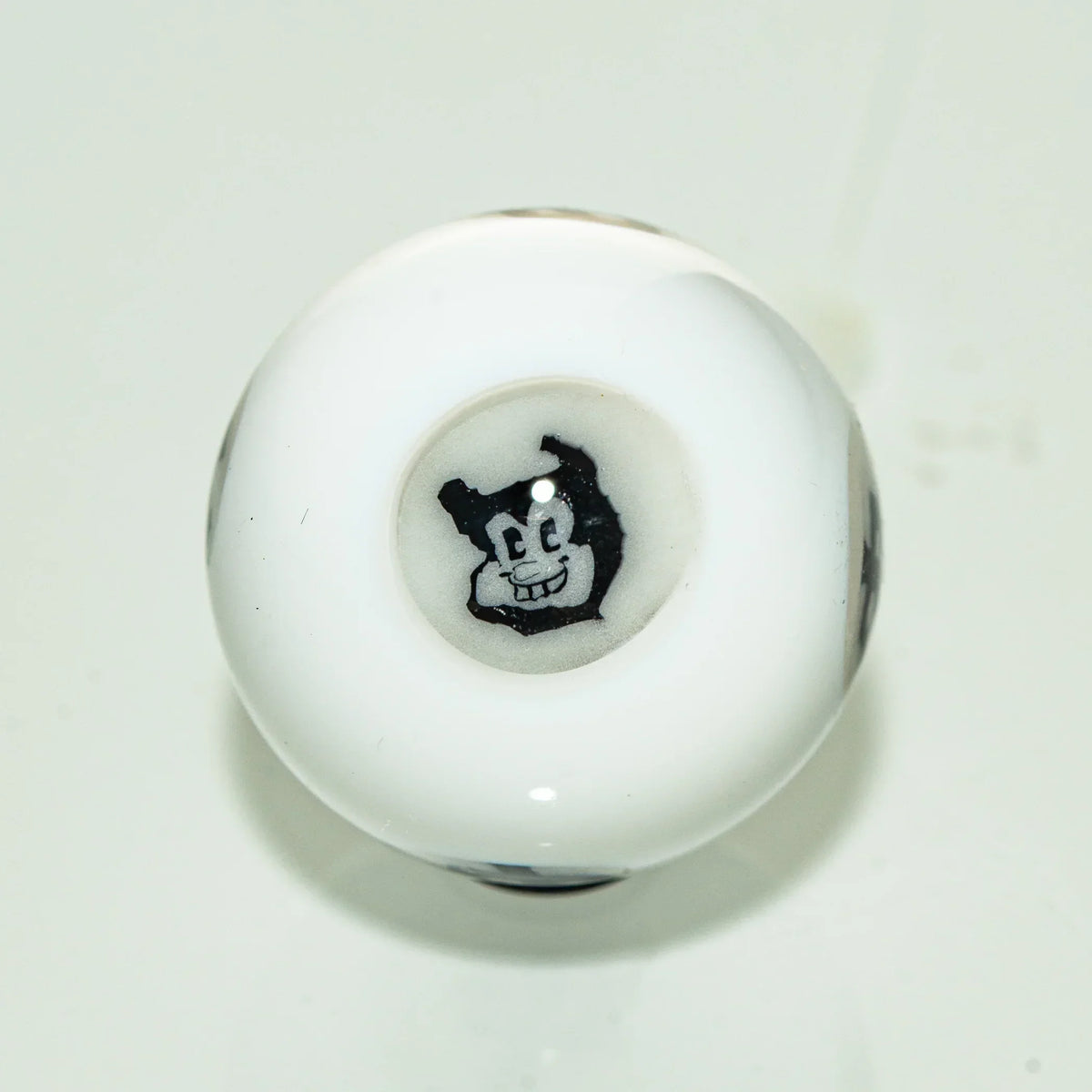 White glass carb cap with cartoon face detail, viewed from above on plain background