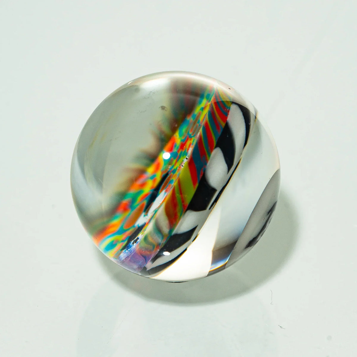 Handcrafted glass marble with colorful cane design and clear accents on a white background