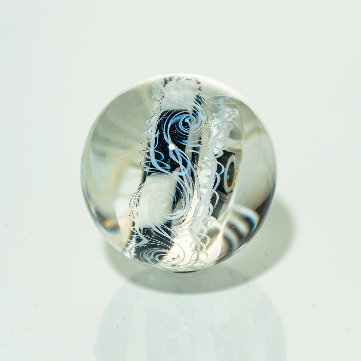 Handcrafted glass marble with intricate white and blue swirling patterns on a clear surface