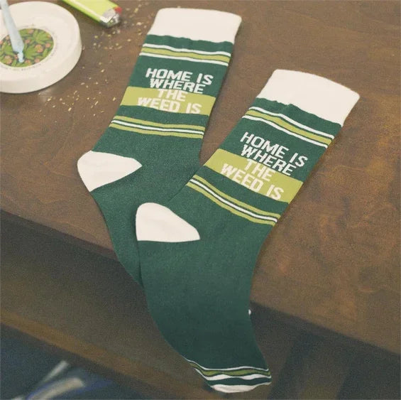 Green and white socks on a table with 'Home is where the weed is' text, cannabis-themed accessory