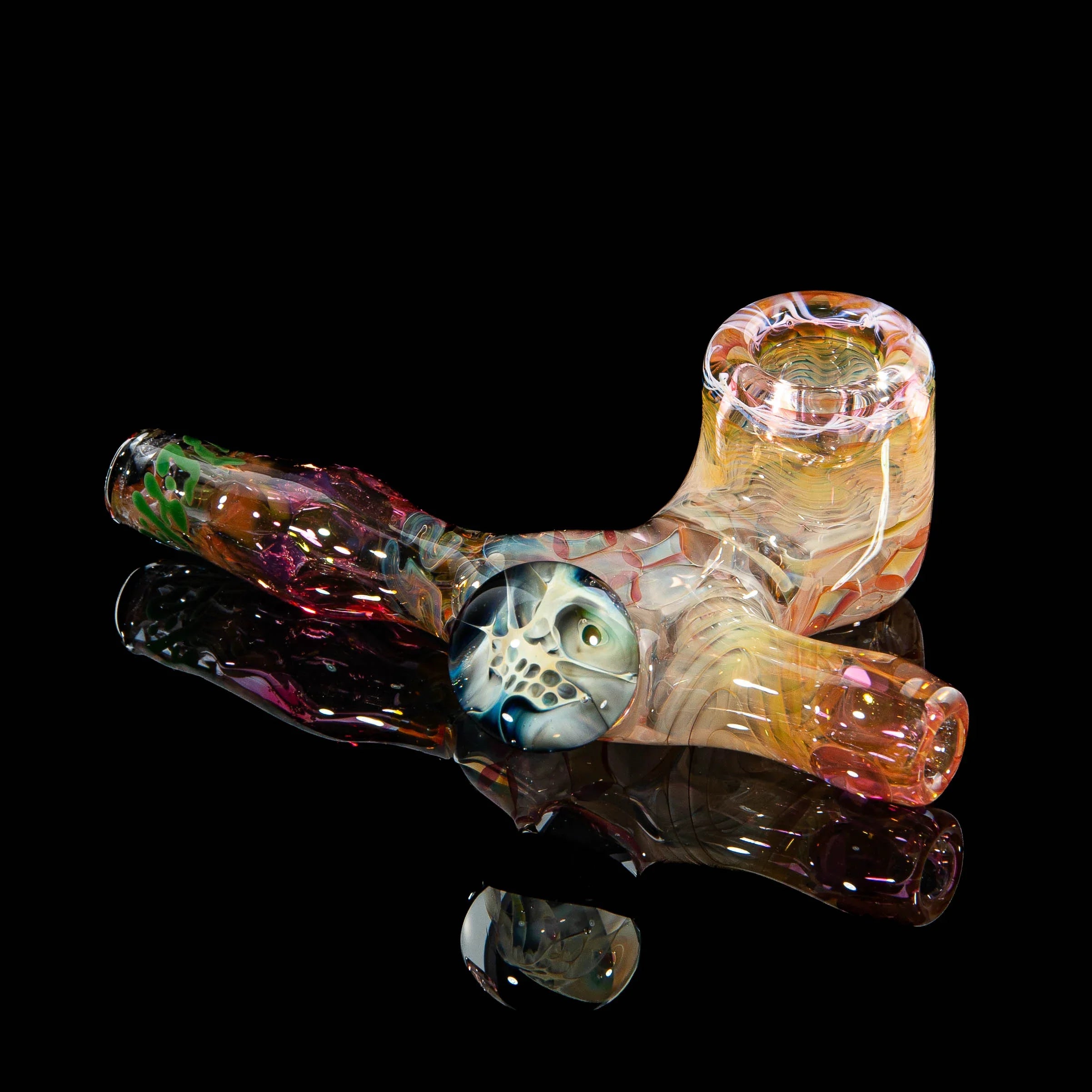 Heady glass hand pipe with colorful swirls and detailed skull design on black background.
