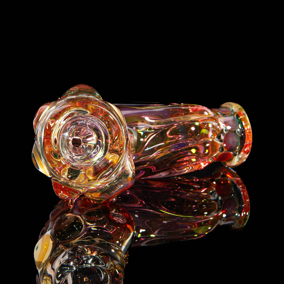 Handblown heady glass pipe with vibrant swirling colors on black reflective surface