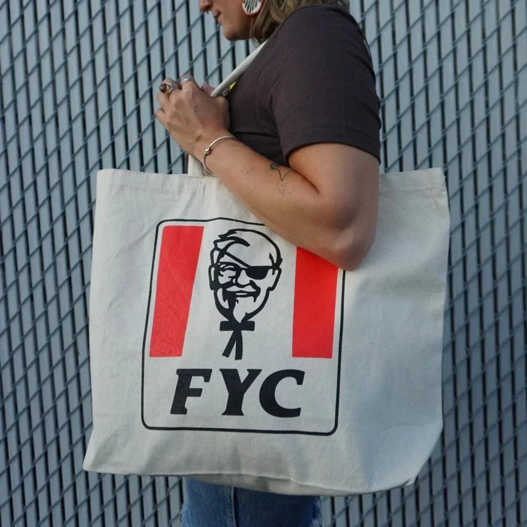 Person holding large canvas tote bag with FYC graphic and red stripes outdoors