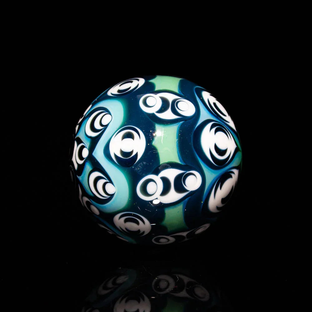Hand-blown glass marble with green, blue, and white psychedelic patterns on black background