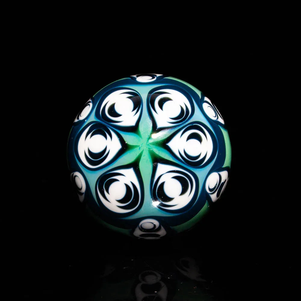 Intricate glass marble with blue, green, and white geometric swirl patterns on black background