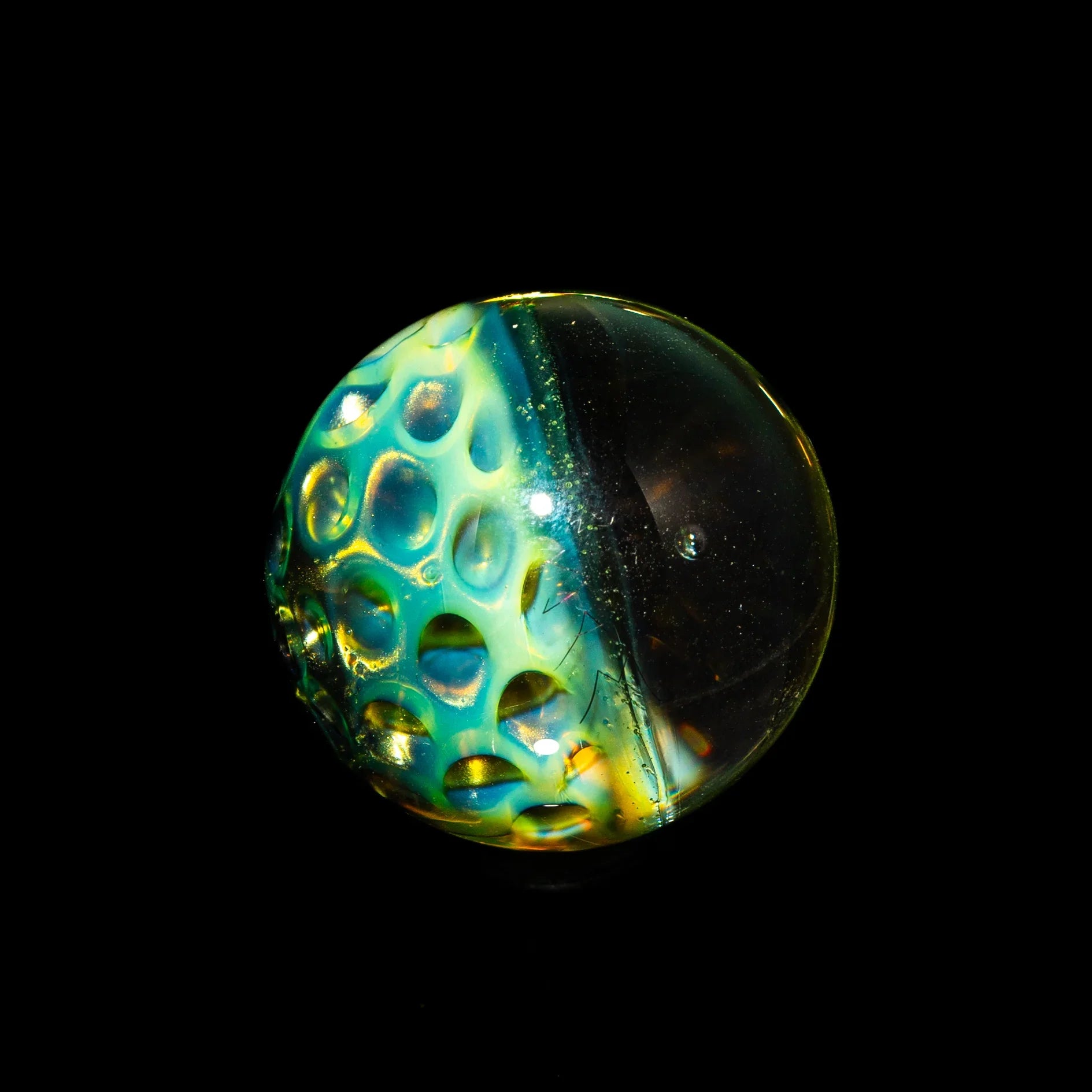 Hand-blown glass marble with honeycomb pattern and vibrant colors on black background