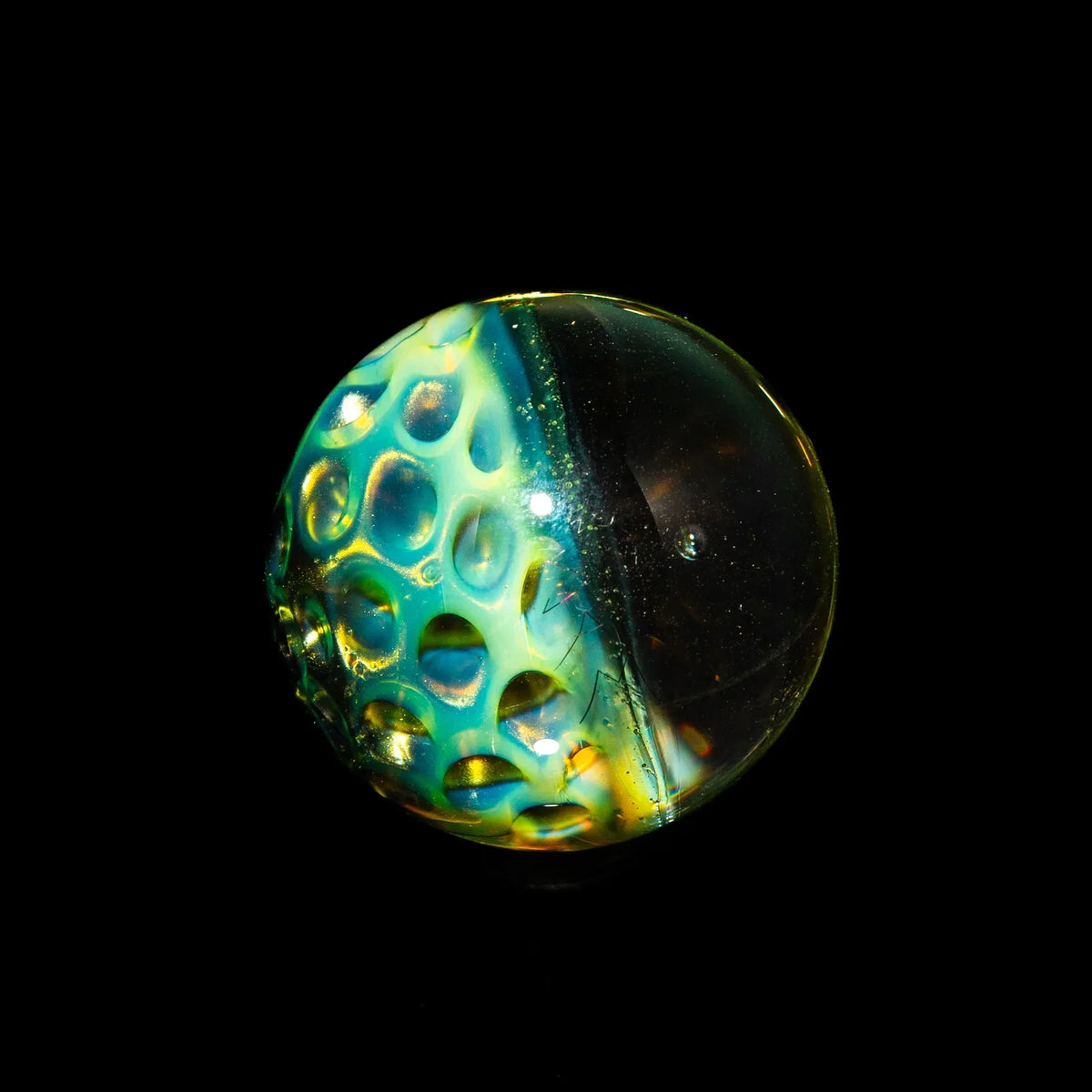 Hand-blown glass marble with honeycomb pattern and vibrant colors on black background